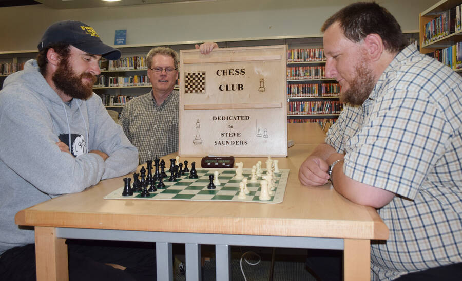 <p>Kevin McBain PHOTO</p><p>Greg Van De Moortele, lead organizer of the Bridgewater Chess Club holds up the chess board holder which he inscribed in honour of founder Steve Saunders, during a recent match between fellow co-ordinators Ryan Weir (left) and David Payne.</p>